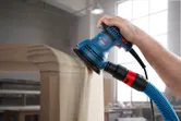 A person uses a random orbit sander on a rounded wooden surface.