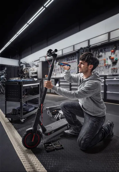 A person repairs an electric scooter using a cordless screwdriver in a workshop.