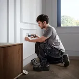 A person uses a cordless screwdriver to install an electrical outlet cover.