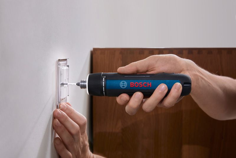 Person using a cordless screwdriver to fasten a screw into a wall switch plate.