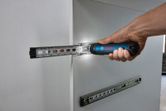 A person uses a cordless screwdriver to install a drawer runner on white cabinetry.