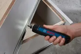 A person uses a cordless screwdriver to assemble a metal cabinet drawer.