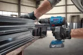 A person wearing safety equipment uses a cordless drill to fasten metal profiles.