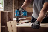 A person wearing safety equipment drills into a wooden board in a workshop.