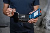 Person holding a cordless LED work light with a battery and metal handle.