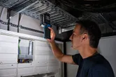 Person inspecting electrical panel using a cordless light in a utility room.