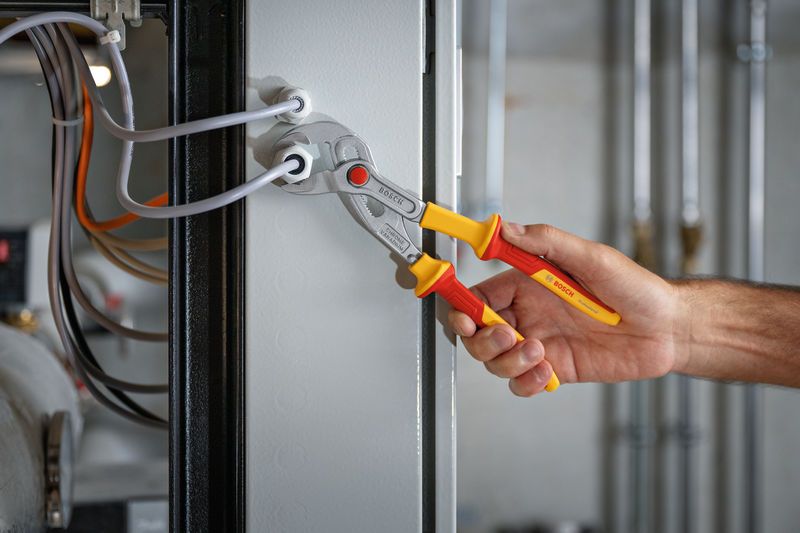 A person uses insulated pliers to work on electrical wiring in a panel.