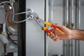 A person uses insulated pliers to work on electrical wiring in a panel.