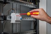 A person tightens a screw on an electrical component in a control panel.