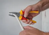 A person uses insulated pliers to grip and bend a thick white cable.