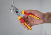 A person cuts an electrical cable using insulated pliers.