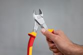 A person holds insulated diagonal side cutter pliers with red and yellow handles.