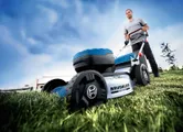 A person pushes a cordless lawn mower over grass in an outdoor area.