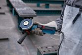 A person wearing safety equipment holds an angle grinder in an industrial setting.