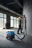 A person wearing safety equipment grinds a concrete wall using an all-purpose extractor.