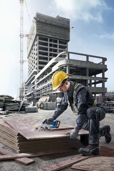 GKS 18V-44 A person wearing safety equipment cuts plywood on a construction site with a cordless saw.