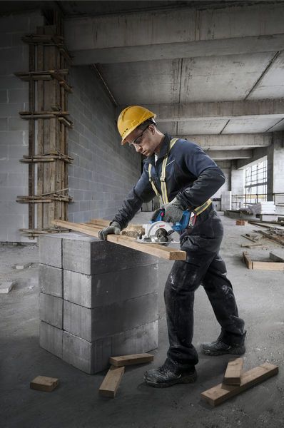 GKS 18V-44 A person wearing safety equipment cuts wood with a circular saw on concrete blocks.