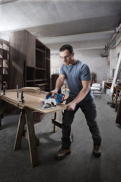 GKS 18V-44 A person wearing safety equipment cuts wood with a cordless circular saw in a workshop.