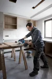 A person wearing safety equipment cuts wood with a circular saw in a kitchen under construction.