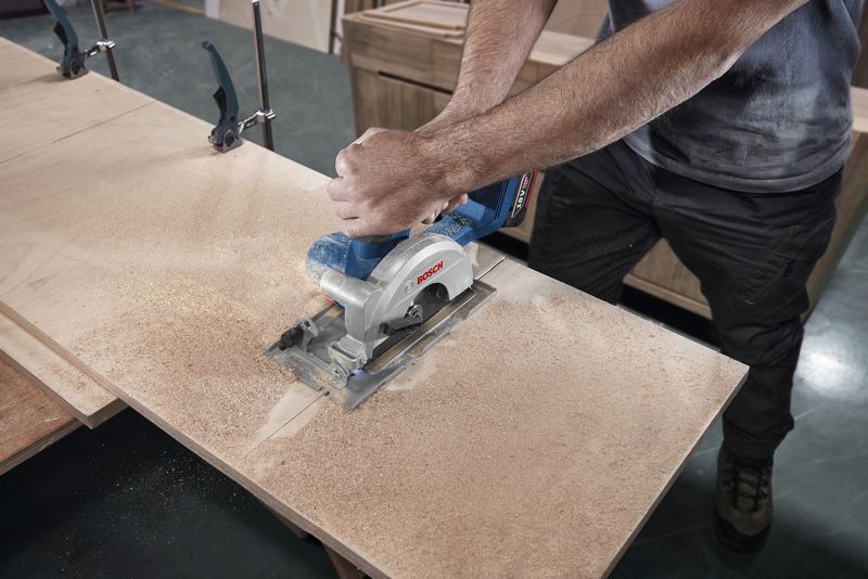 GKS 18V-44 A person cuts plywood with a circular saw in a woodworking shop.