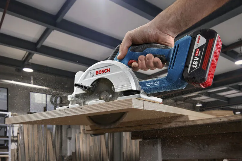 A person cuts wood with a cordless circular saw in a workshop.