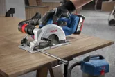 A person wearing safety equipment uses a circular saw to cut a wooden board.