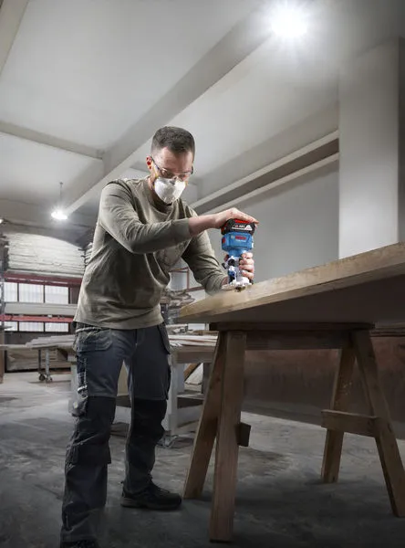 GLF 18V-8 A person wearing safety equipment uses a router on the edge of a wooden table.