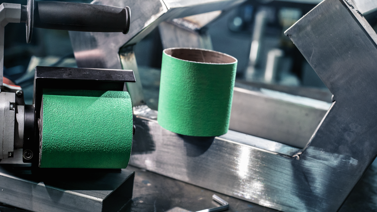 Green sanding drum tool and sanding sleeve placed on a metal workbench.