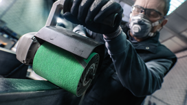 Person wearing safety equipment polishes a metal surface with a power sander.