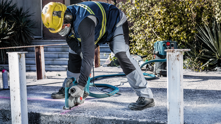 Object #200456641: 3087975_app_web_04 A person wearing safety equipment cuts concrete with a power saw outdoors.