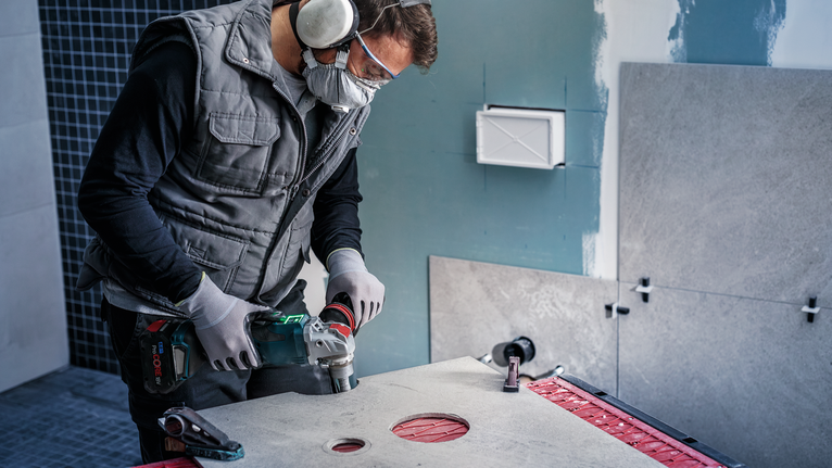 Person wearing safety equipment drills a hole in a large tile.