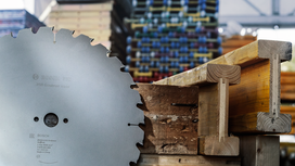 Large circular saw blade beside a wooden beam in a workshop.