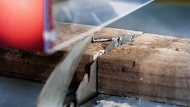 Circular saw cutting through a wooden plank with a metal screw embedded.