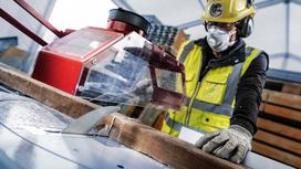 A person wearing safety equipment guides wood through a table saw.