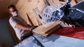A person wearing safety equipment cuts wood with a table saw.