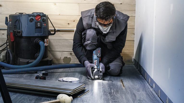 PRO ACZ 85 EIB Multitool Blade, 85 mm A person wearing safety equipment cuts laminate flooring with a power tool.