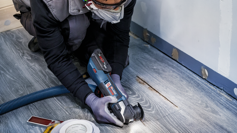 PRO ACZ 85 EIB Multitool Blade, 85 mm Person wearing safety equipment cuts a wooden floor with a power tool.