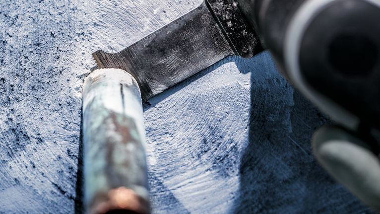 Person wearing safety equipment cuts through a metal pipe with a reciprocating saw.