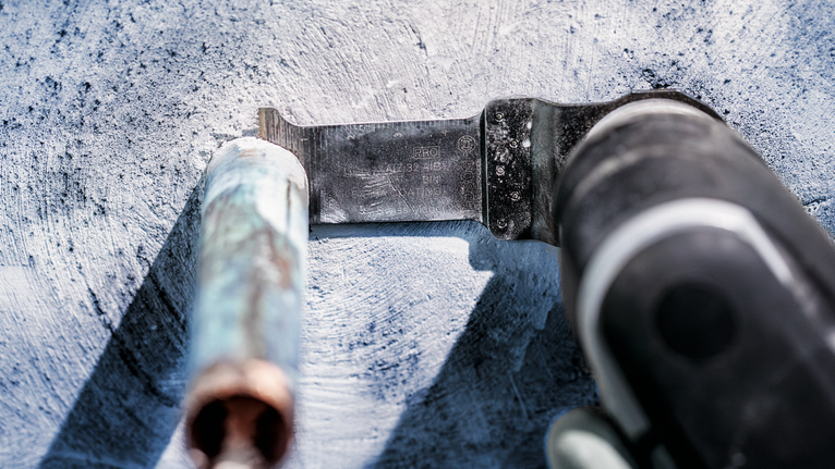 Oscillating tool cuts through a metal pipe on a concrete surface.