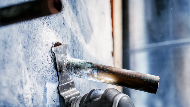 Power tool cuts through a metal pipe protruding from a concrete wall.
