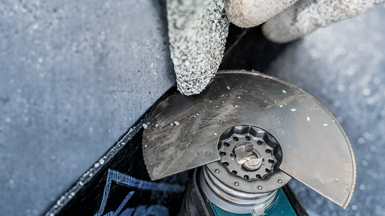A person wearing safety equipment cuts concrete with an angle grinder.