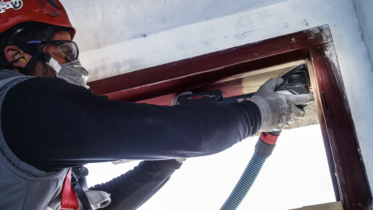 PRO AVZ 93 G Multitool Accessory, 93 mm Person wearing safety equipment sanding a wooden window frame with a power tool.