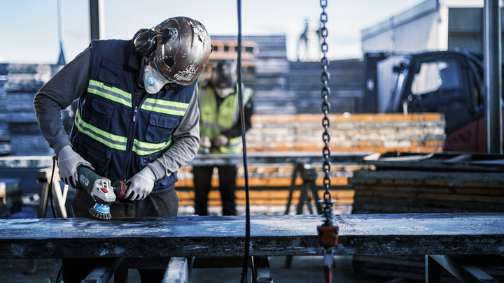 Object #200456904: 3089943_app_web_01 Person wearing safety equipment grinds a metal beam at a construction site.