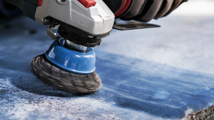 Object #200456908: 3089943_app_web_05 Person wearing safety equipment grinds a blue stone surface with a wire cup brush.