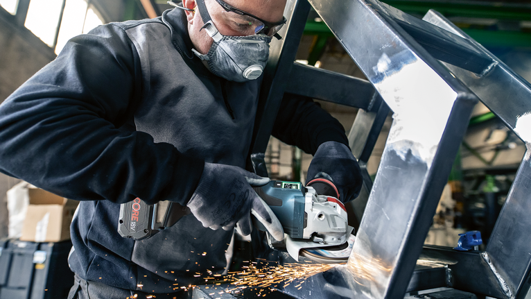 PRO X571 Flap Disc, Angled, 125 mm, G40, X-Lock A person wearing safety equipment grinds a metal frame, producing sparks.