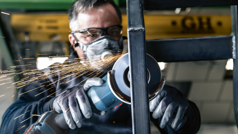 PRO X571 Flap Disc, Angled, 125 mm, G40, X-Lock Person wearing safety equipment grinds metal, creating sparks.