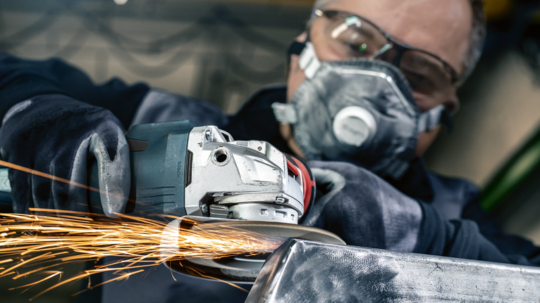 PRO X571 Flap Disc, Angled, 125 mm, G40, X-Lock A person wearing safety equipment grinds metal, creating bright sparks.