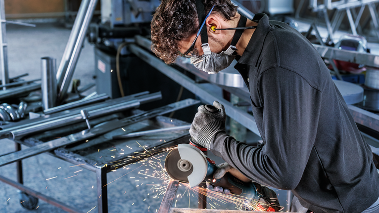 PRO Stainless Steel and Metal Bonded Cutting Disc, 125 x 1 x 22.23 mm, X-Lock, Straight Person wearing safety equipment uses an angle grinder to cut metal, producing sparks.