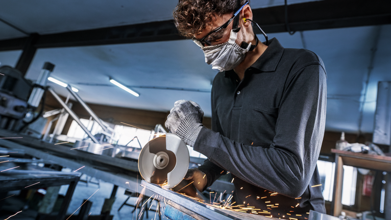 PRO Stainless Steel and Metal Bonded Cutting Disc, 125 x 1 x 22.23 mm, X-Lock, Straight Person wearing safety equipment cuts metal with an angle grinder, sparks flying.