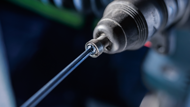 Close-up of a power drill driving a screw into a surface.